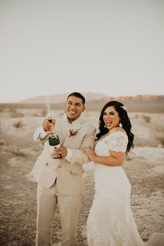 groom spraying champagne, bride holding his arm and smiling