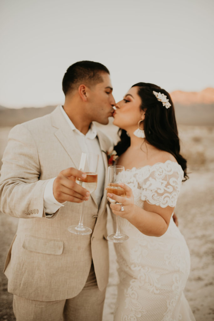 bride and groom kissing while holding champagne glasses