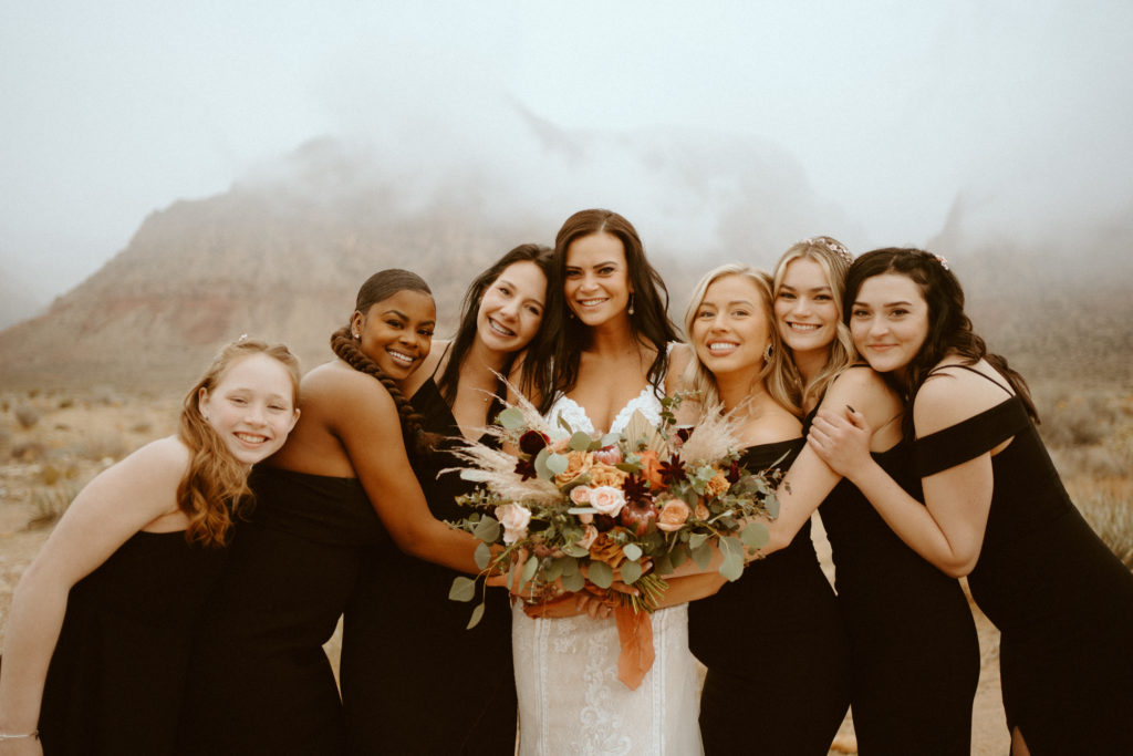 Bride with sage and peach bouquet with wedding party in all black bridesmaids dresses in Red Rock Canyon for Red Rock Bridals & Simple Affair Micro-Wedding 