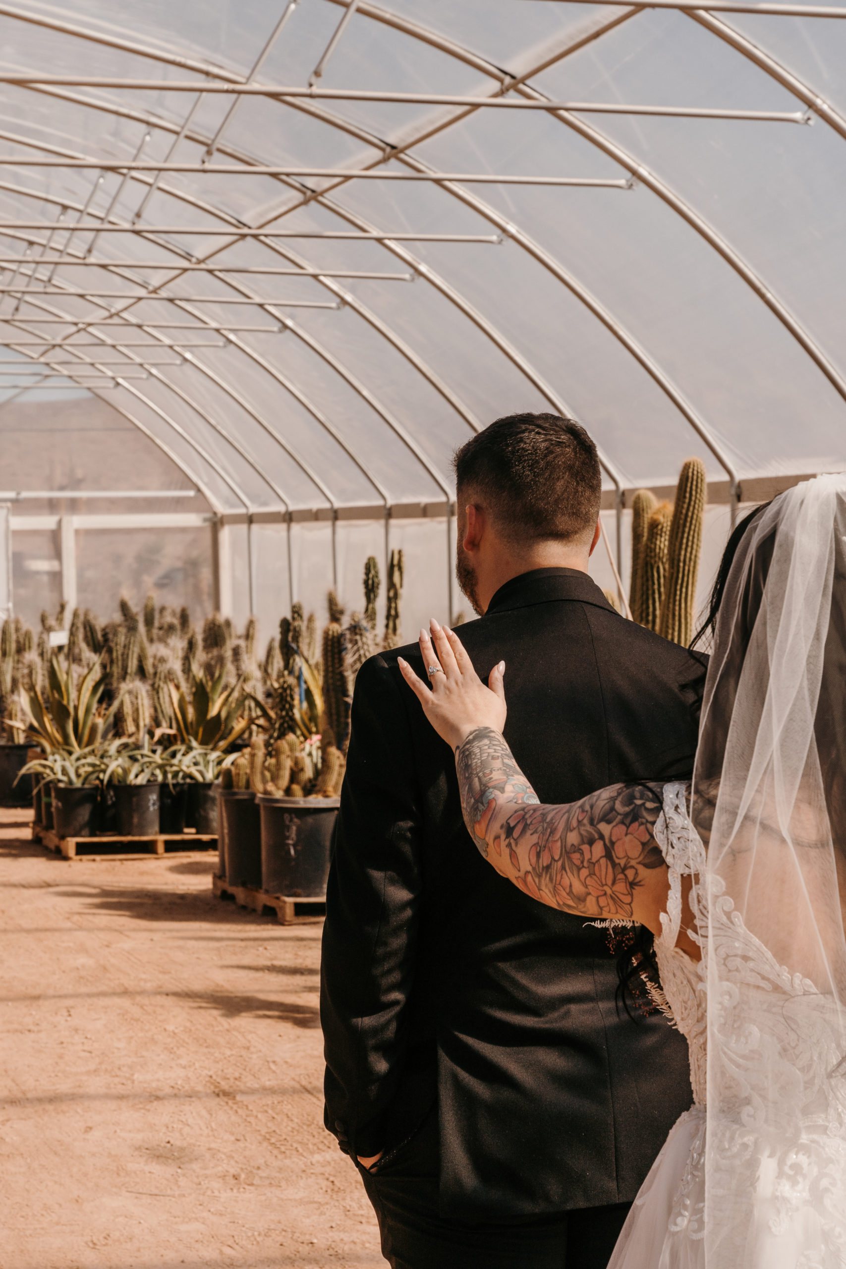 Bride touching groom's shoulder for him to turn around for first look in cactus greenhouse 