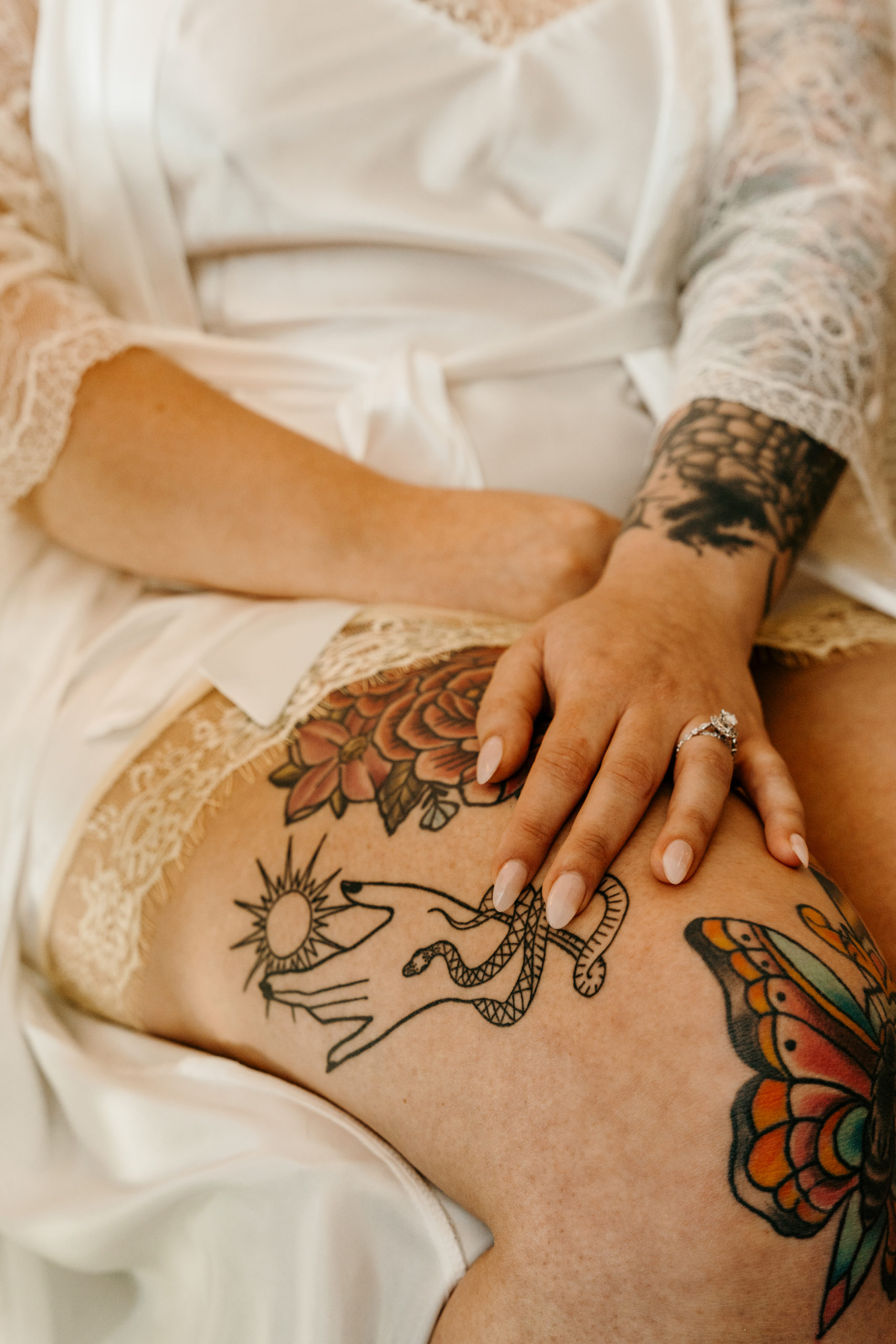 Bride in robe getting ready with her hand on tattooed leg showing engagement ring and manicure 