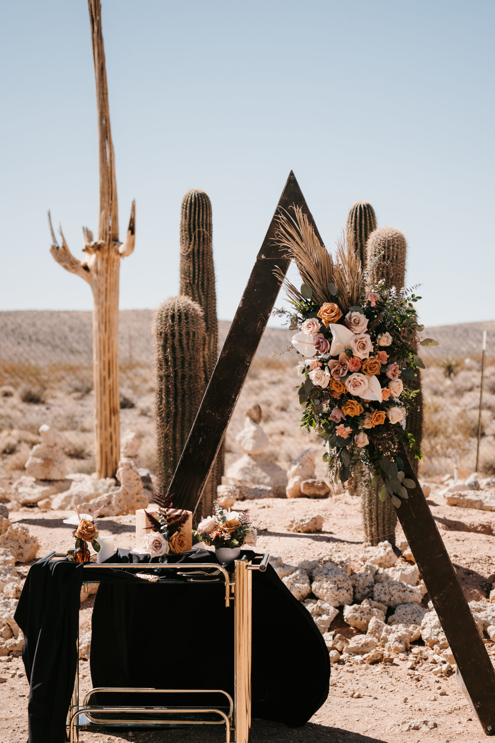 Cake Table with blushes, beiges, and true blacks next to Ceremony arch in Modern-Boho Las Vegas Elopement