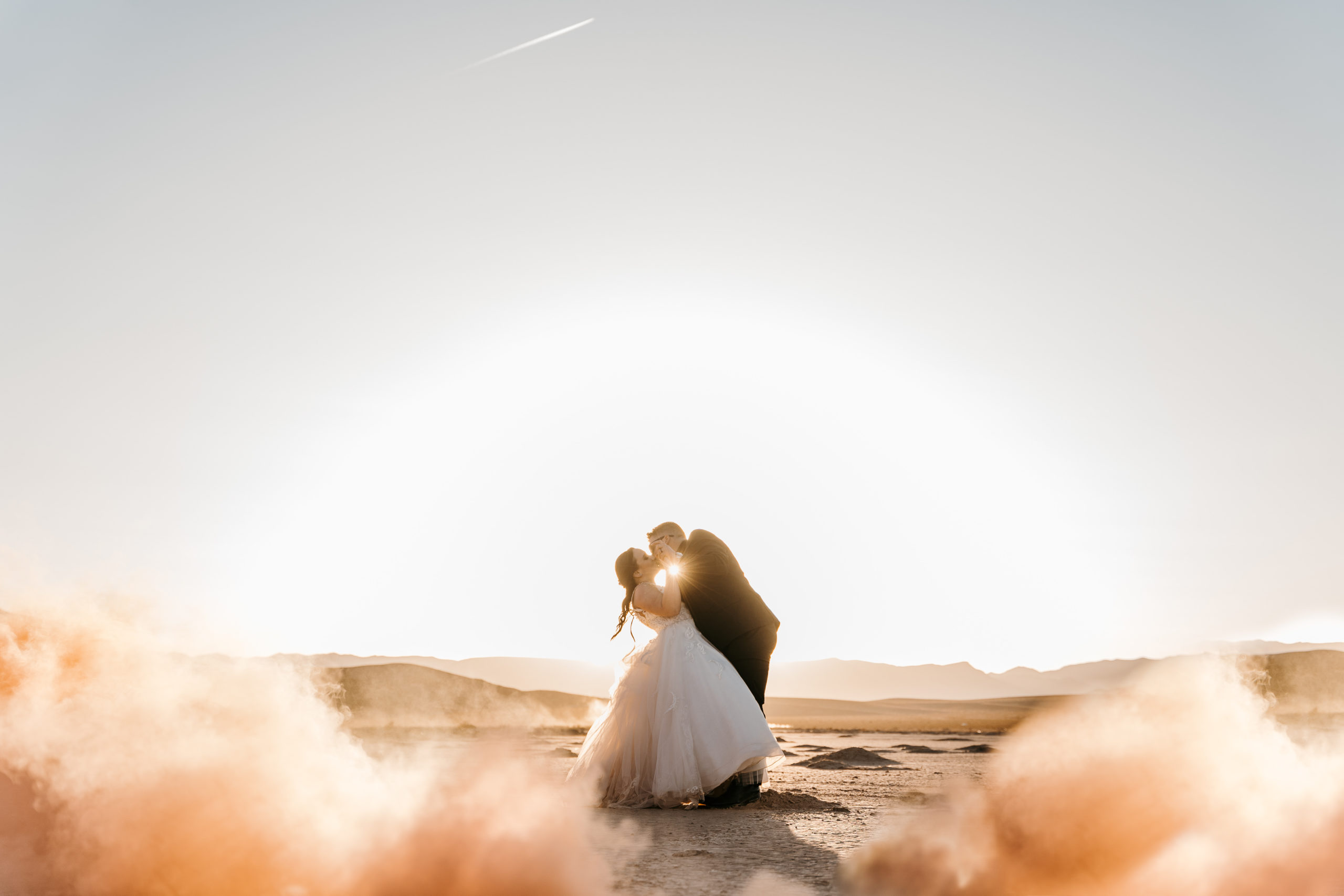 Couple surrounded by smoke bomb on dry lake bed with sunset beaming behind them after Modern-Boho Las Vegas Elopement