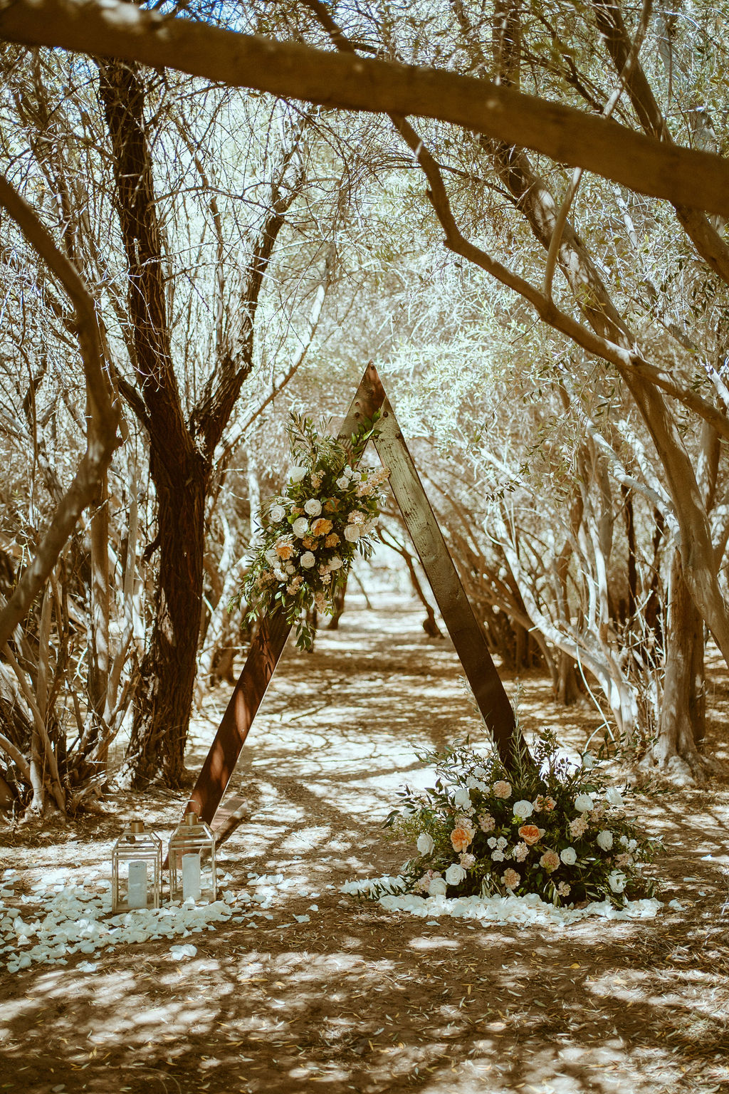 Ceremony triangle arch with two florals pieces, flower pedals, and two lanterns 