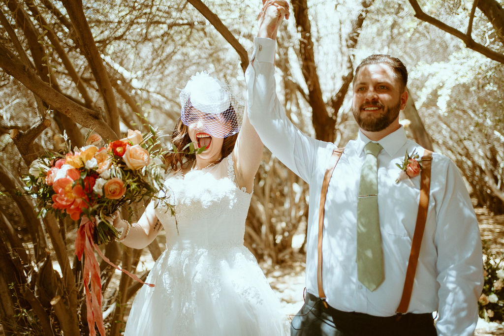 Newlyweds holding hands and putting them in the air smiling after first kiss 