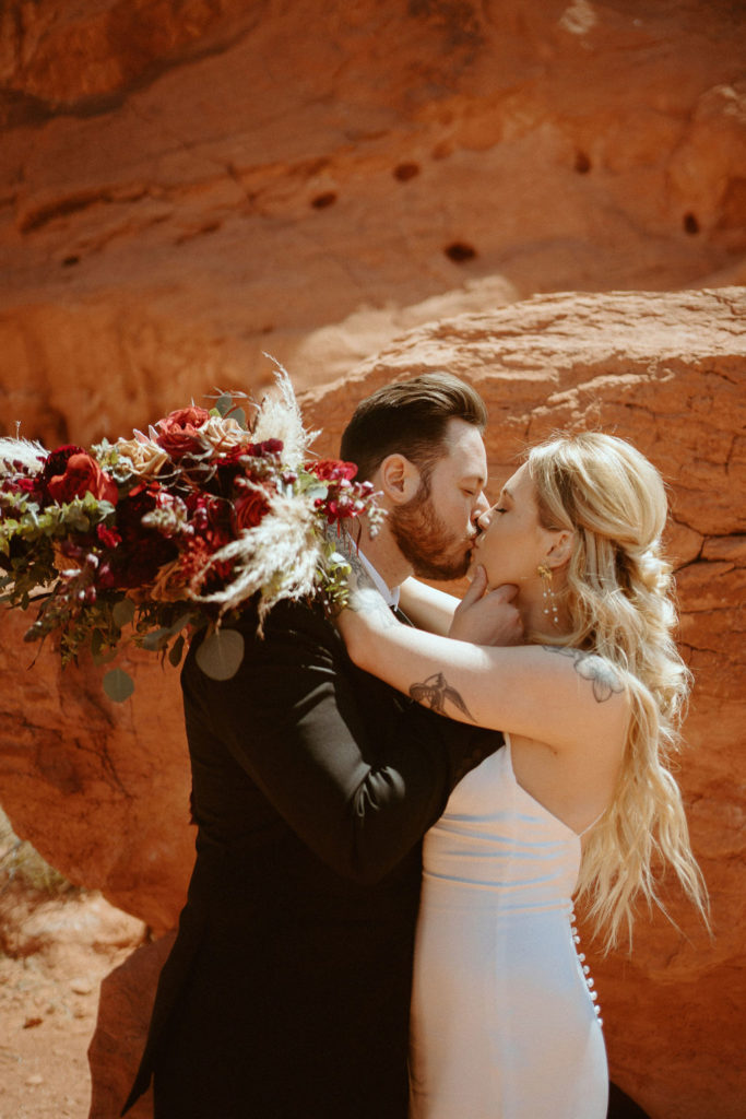 Couple is kissing with brides arms wrapped around grooms neck with moody bohemian florals 