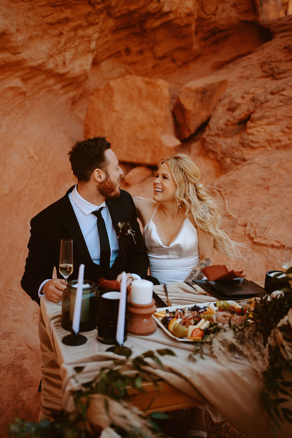 Bride and Groom laughing at decorated sweetheart table in Valley of Fire while wind is blowing 