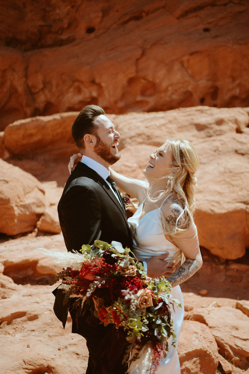 Bride and groom laughing together with Brides Moody Bohemian Bouquet in desert 