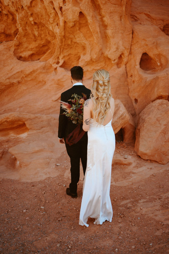 Bride is tapping on Groom's shoulder for first look during their moody bohemian desert elopement 