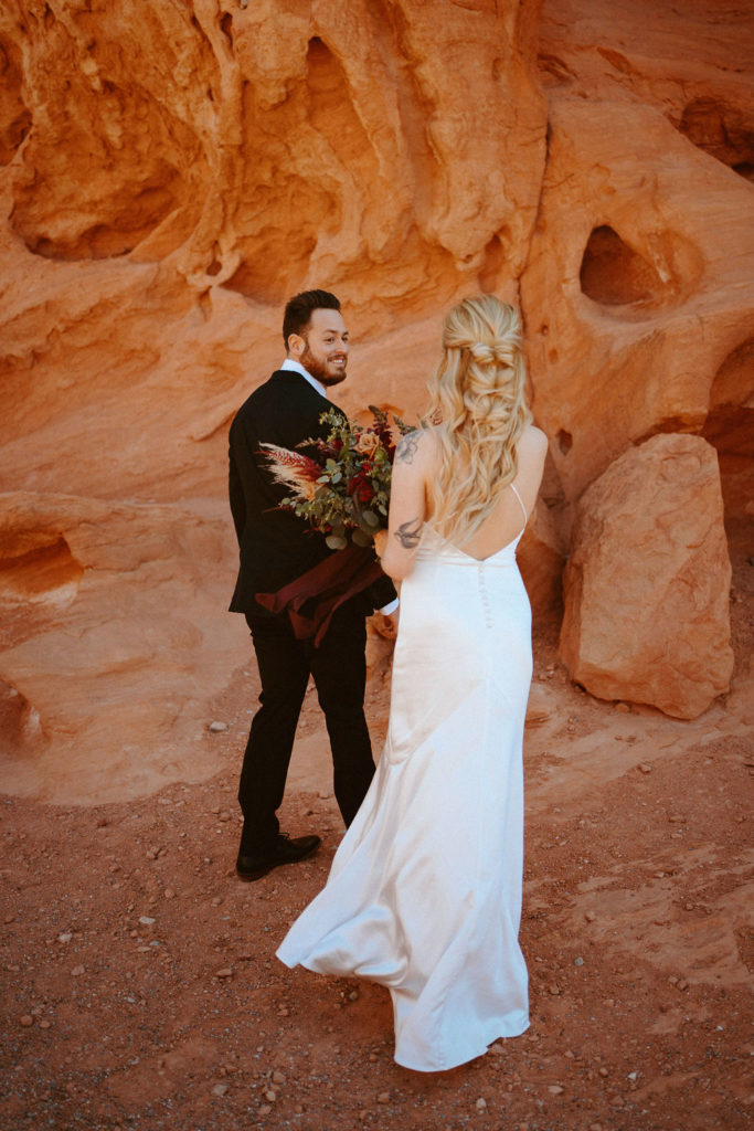 Groom is smiling while turning around for first look near rocks