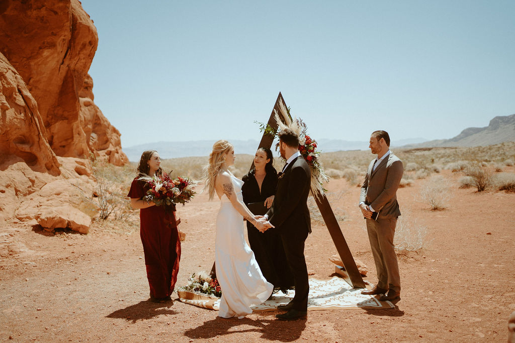 Bride and Groom standing under arch with officiant, best man, and maid of honor 