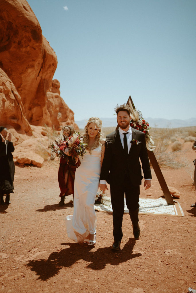 Bride and groom walking down aisle after first kiss in moody bohemian desert elopement 