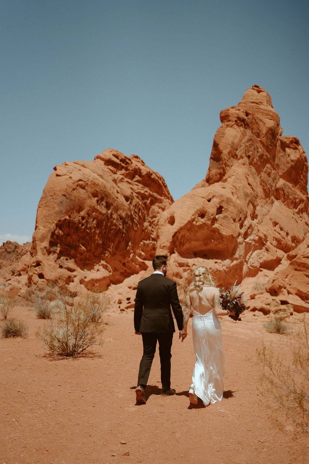 Bride and groom walking away from ceremony after getting married at valley of fire las vegas with dramatic rocky background 