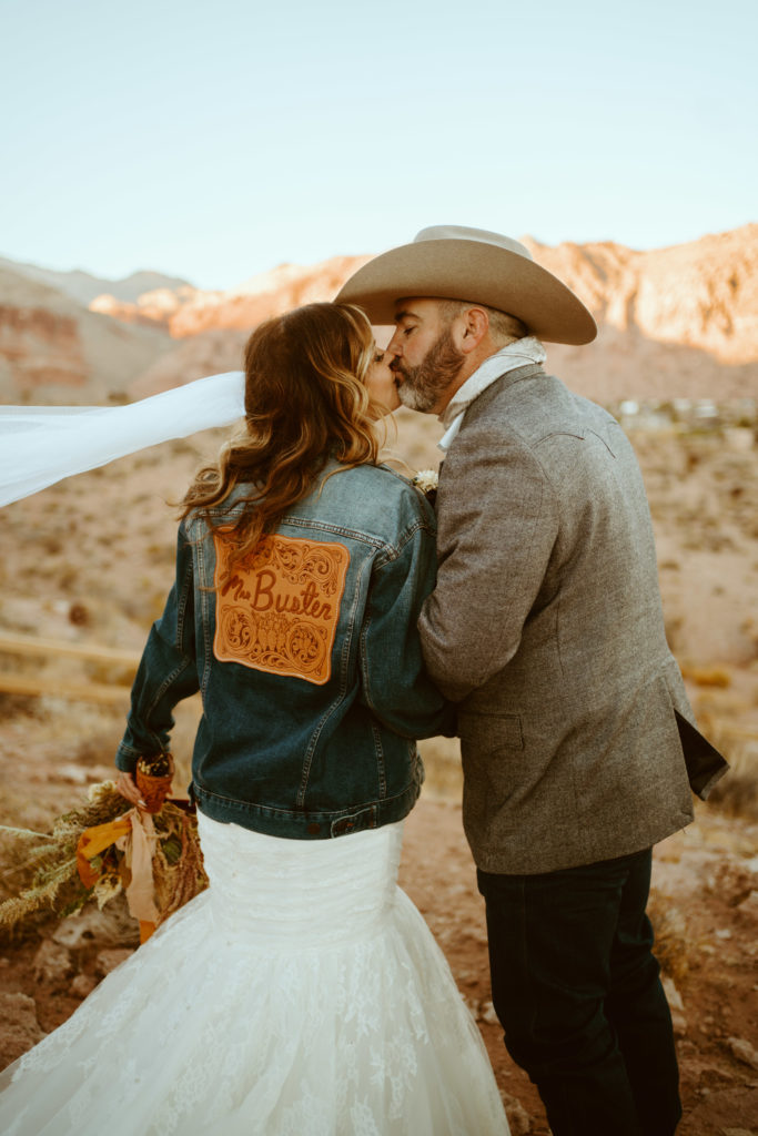 bride wearing customized jean jacket as statement wedding accessory while kissing groom