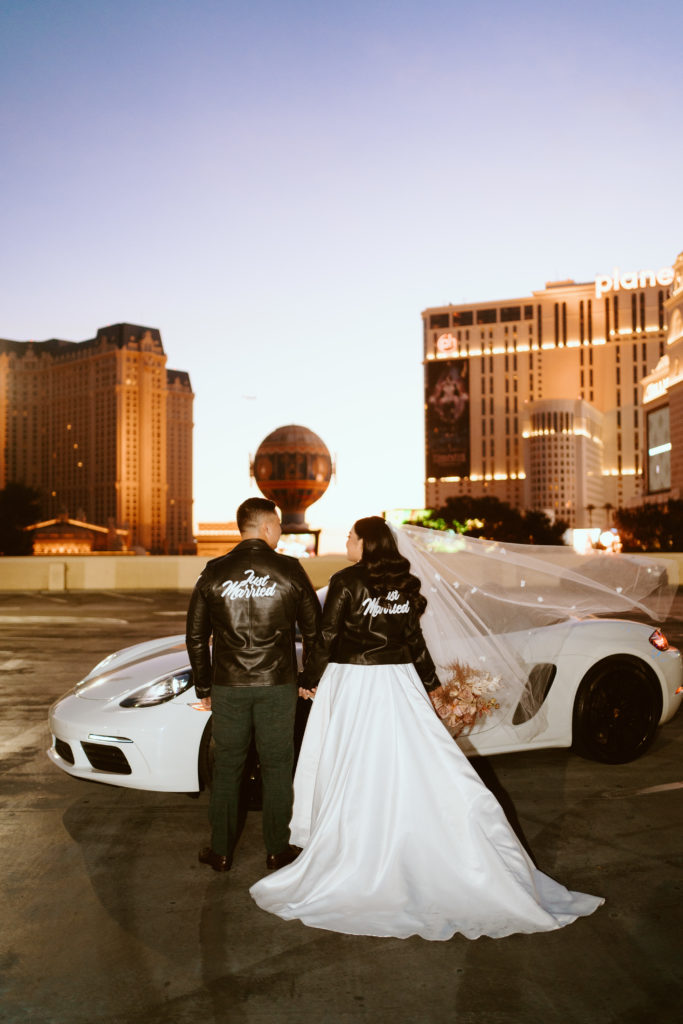 bride and groom looking at each other while holding hands wearing leather jacket 