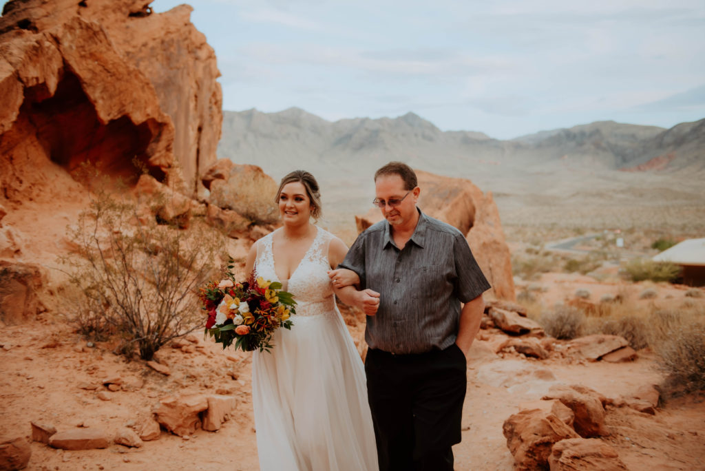 Bride smiling walking down the aisle with father during elopement in desert 