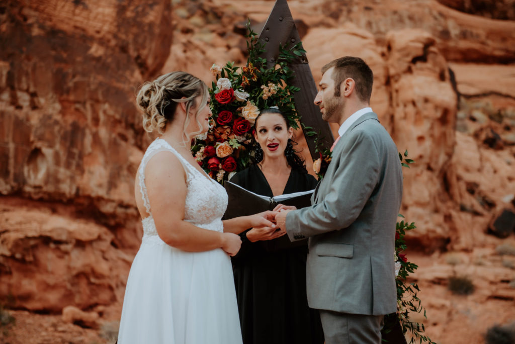 bride and groom with officiant getting married under fall themed bohemian arch 