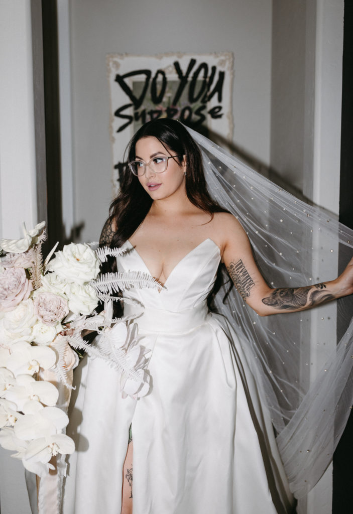 bride holding veil smiling into distance wearing white framed glasses as her statement wedding accessory 