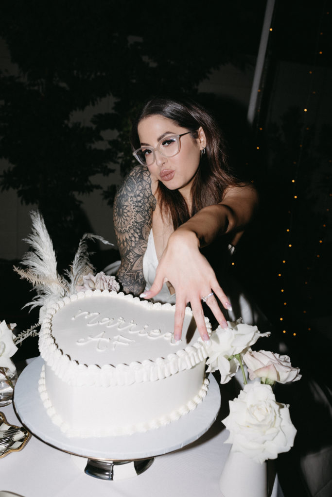 bride holding hand showing off ring next to cake 