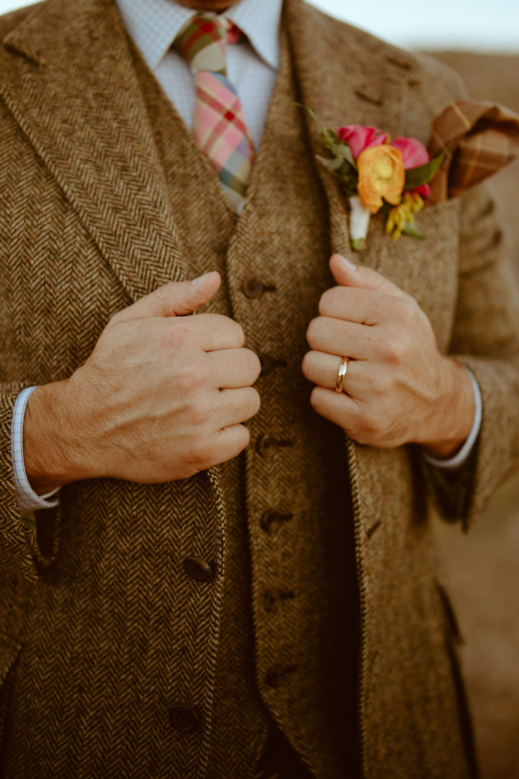 Groom in brown tweed suit and plaid wedding tie with bright and bold pink  boutonnière