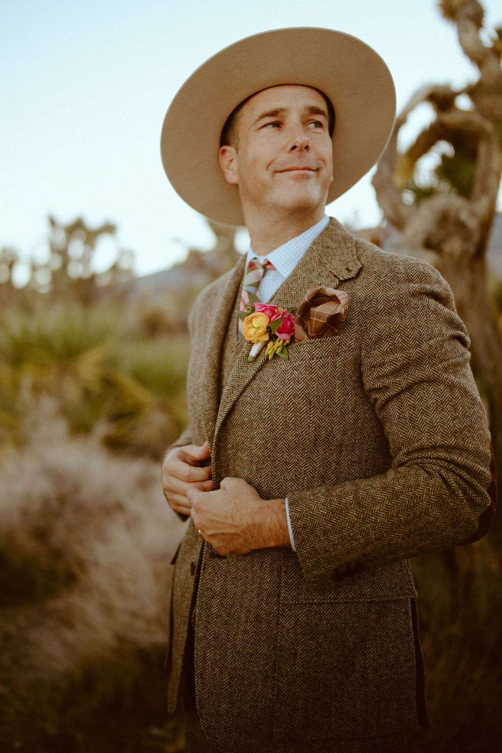 Groom in brown tweed suit and plaid wedding tie with bright and bold pink and mustard boutonnière