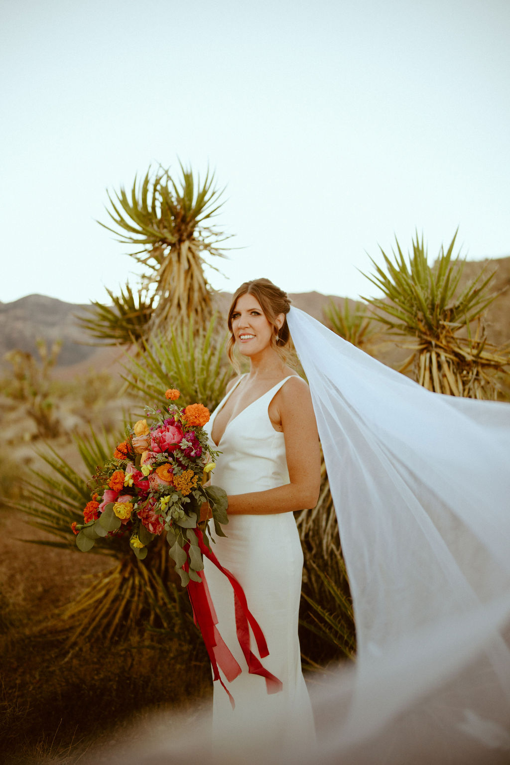 Bride with long white veil holding bright and colorful bouquet 