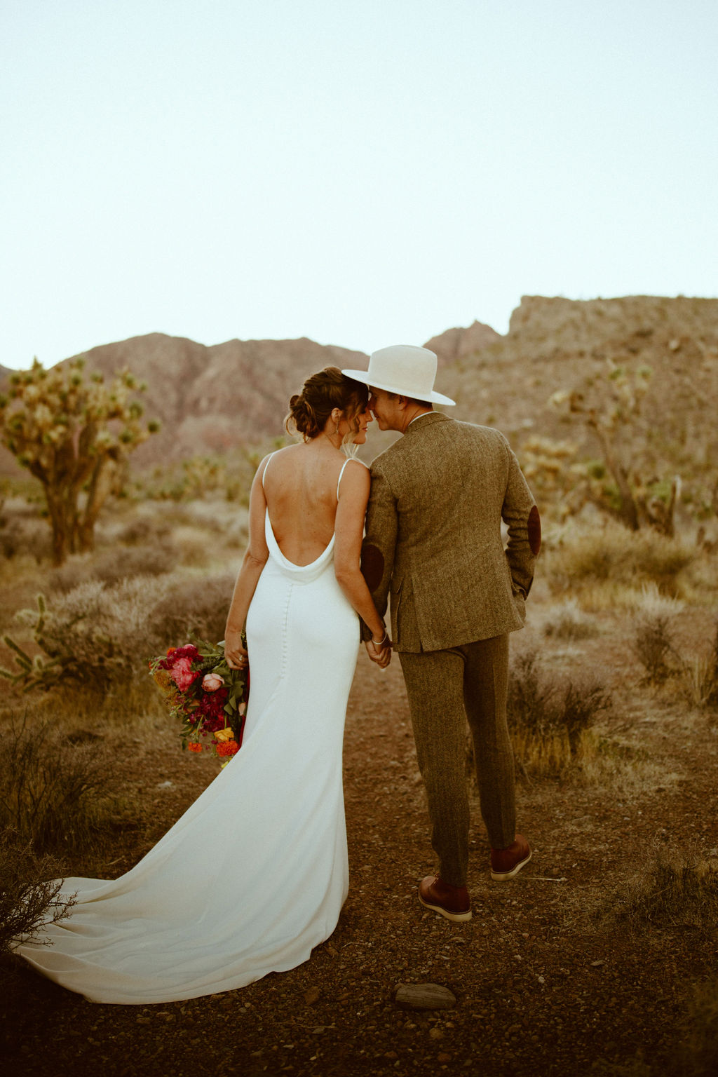 Bride in white backless gown with Groom in brown tweed suit and cream colored hat 