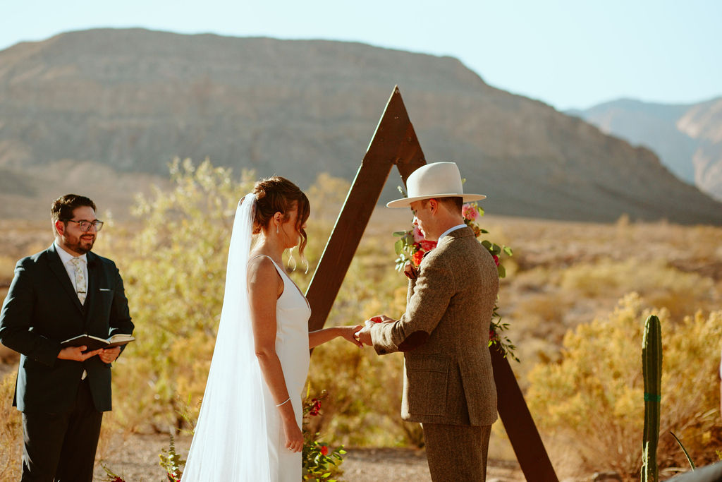 Groom in large brim fedora hat and bride in white gown with long veil getting married in Las Vegas desert 