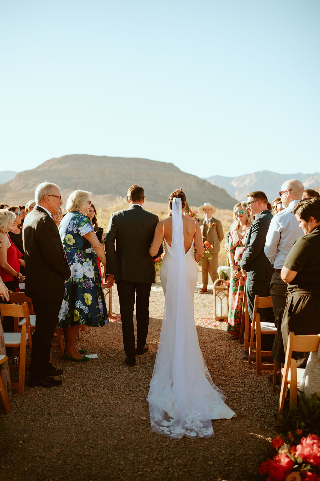 Bride wearing beautiful white gown with bridal train walking down the aisle with her father in desert wedding 