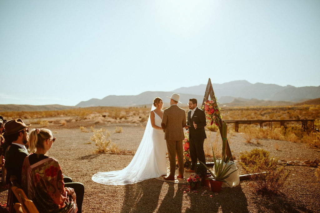 Couple stating at altar under Triangle Arch during Bright & Bold Sunset Desert Wedding 