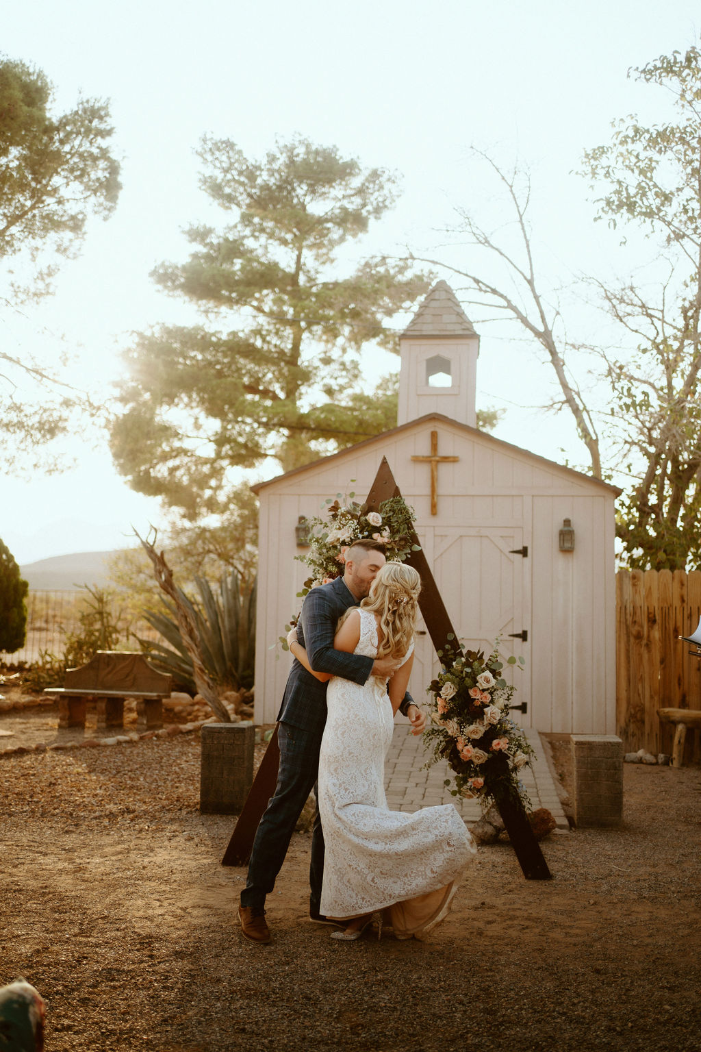Bride and Groom Kissing Near Chapel and Triangle Arch with Florals at Cactus Joe's Micro-Wedding