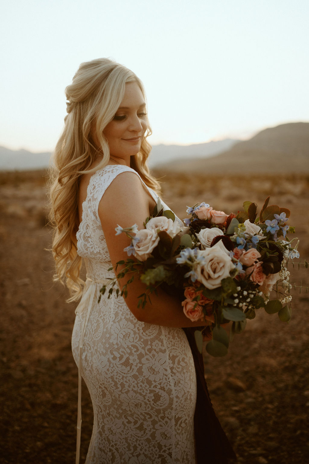 Bride holding looking at Bouquet that is Dusty Blush, Dusty Blue, Off-white, Eucalyptus, Sage Green 