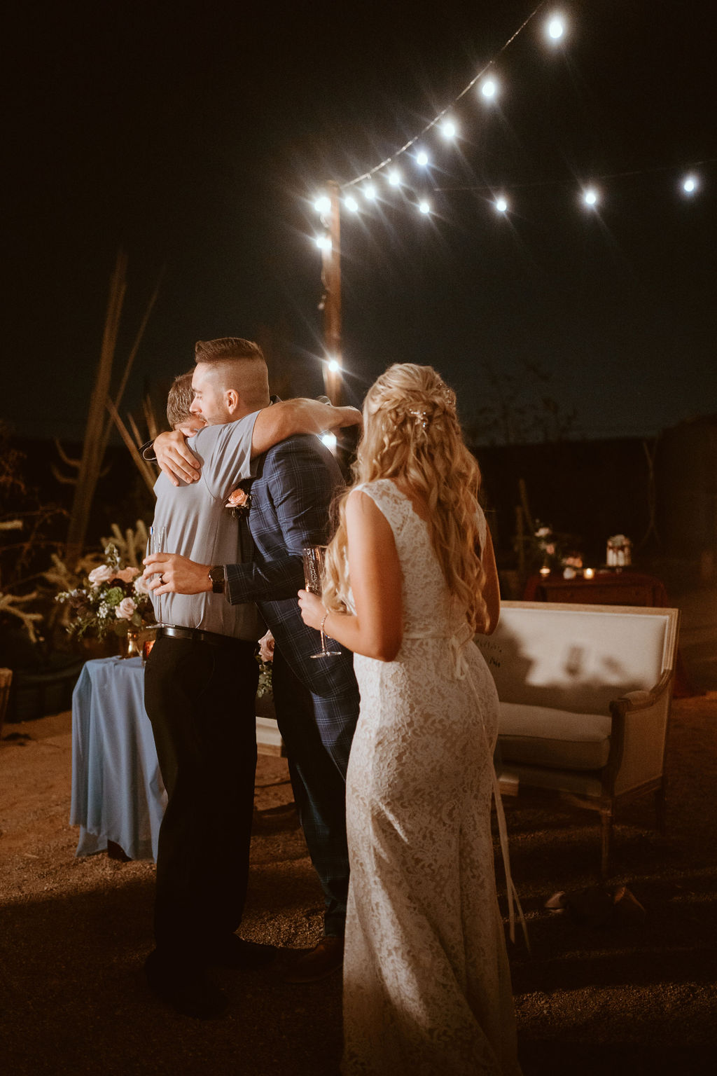 Man Hugging Groom during Outdoor Wedding Reception 