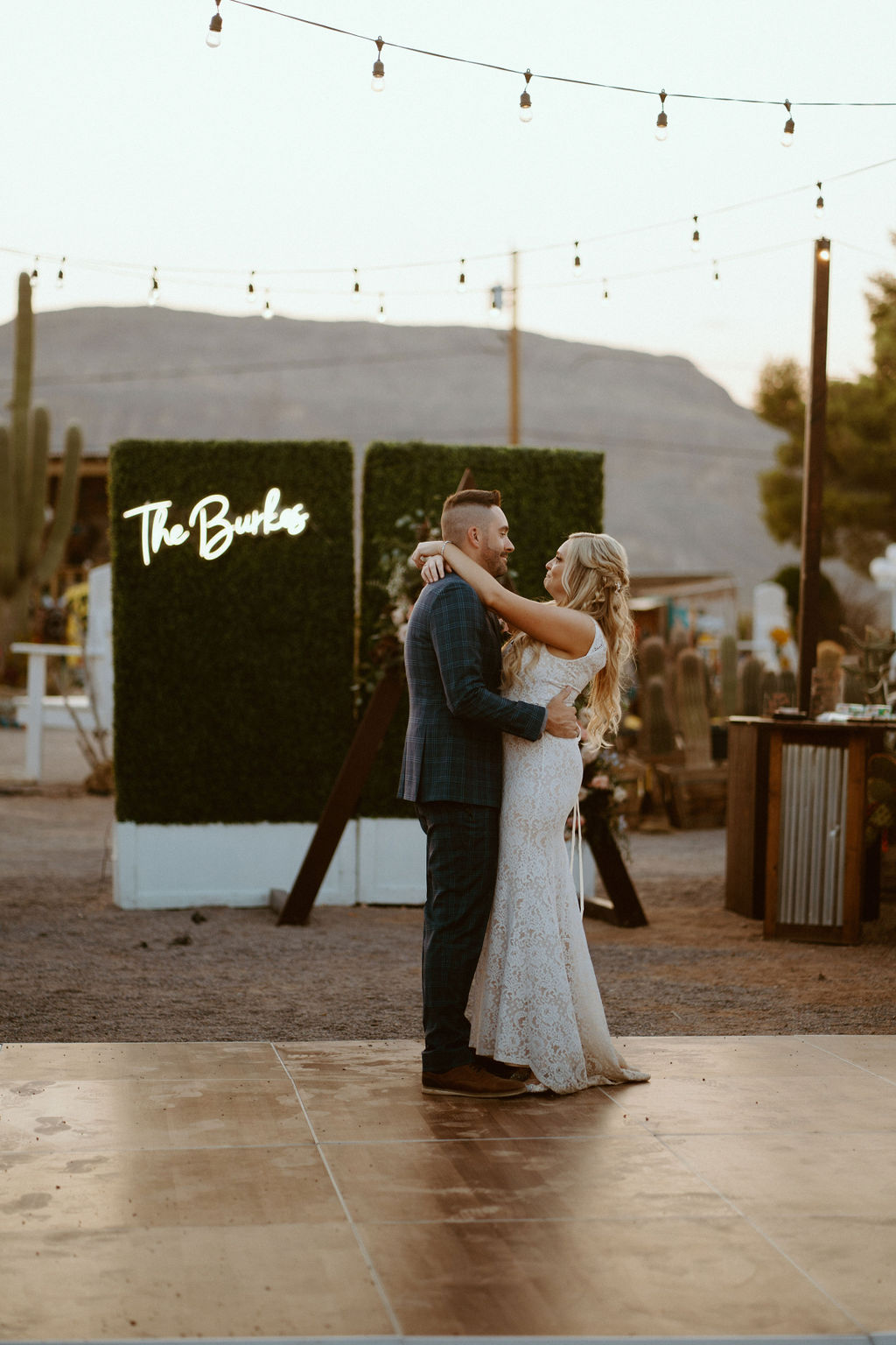 Bride and Groom Begin First Dance with Bistro Lighting & Neon Sign in the Background 