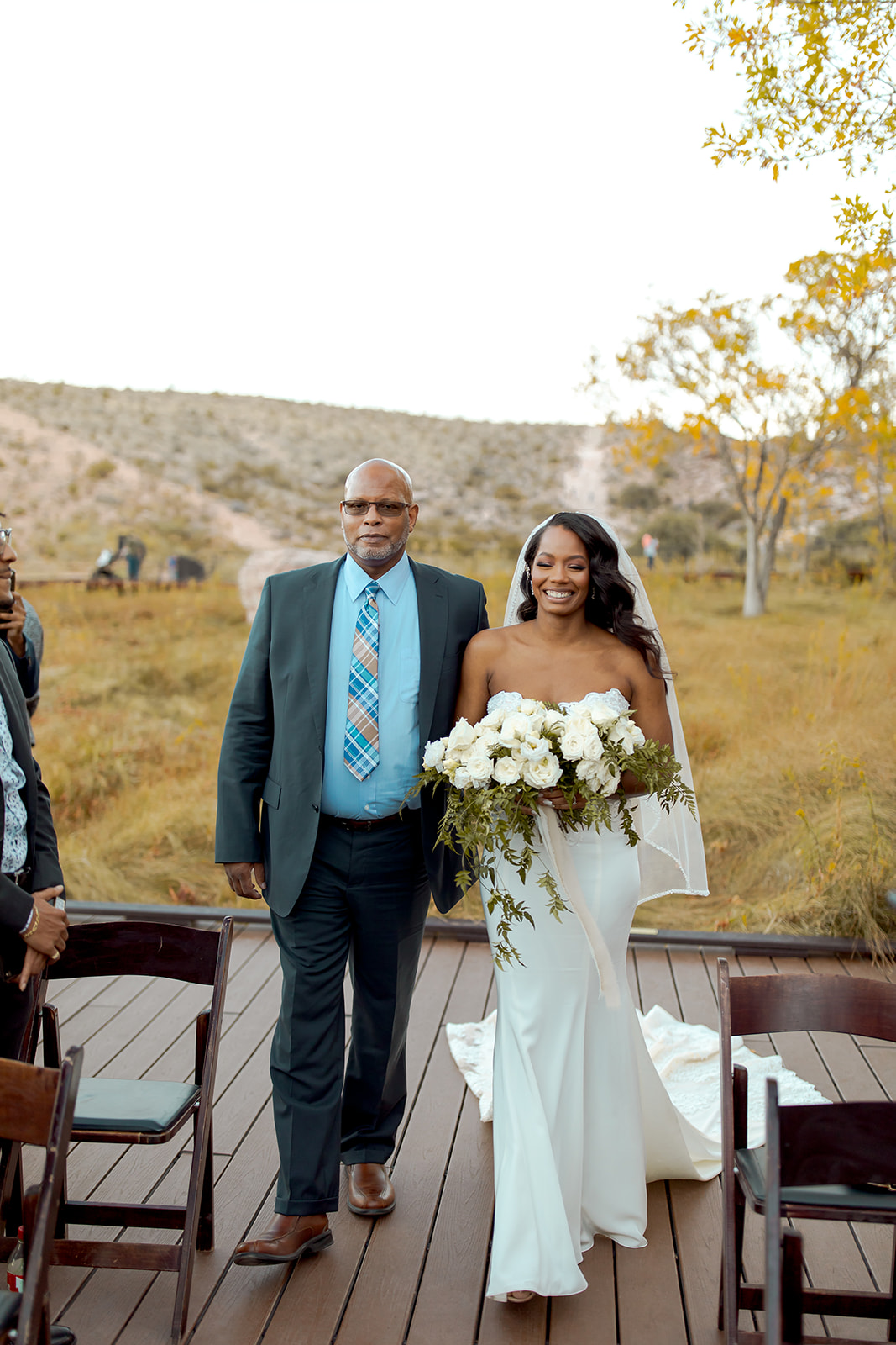 Bride with white rose bouquet and greenery with father smiling walking down aisle for Calico Basin Red Springs Autumn Elopement  