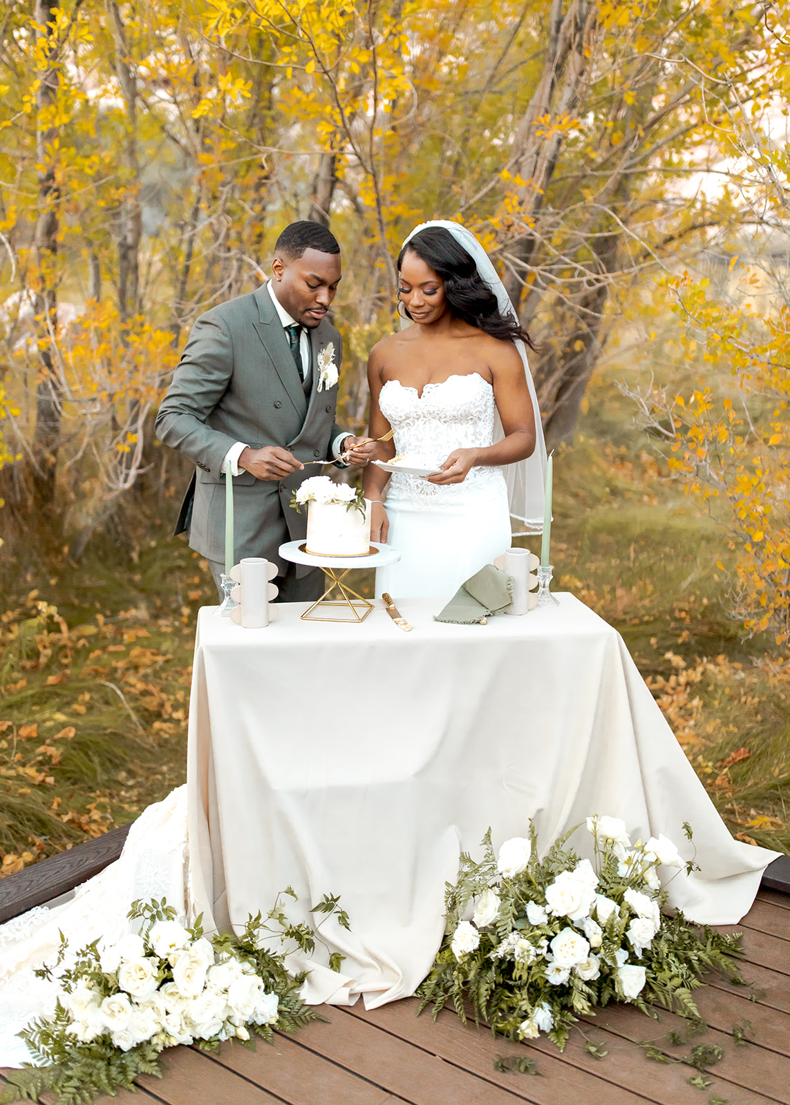 Couple cutting cake with yellow fall leaves behind them 
