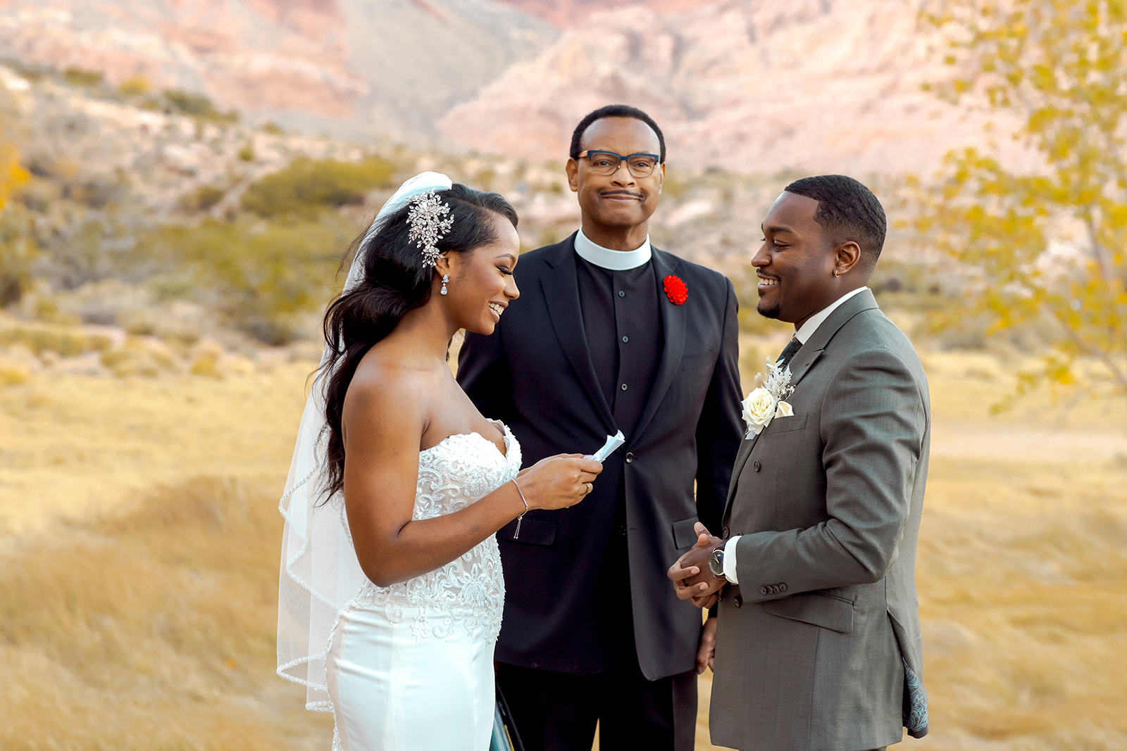 Bride reading vows and smiling for Calico Basin Red Springs Autumn Elopement with white, sage, gold, and greenery fall theme