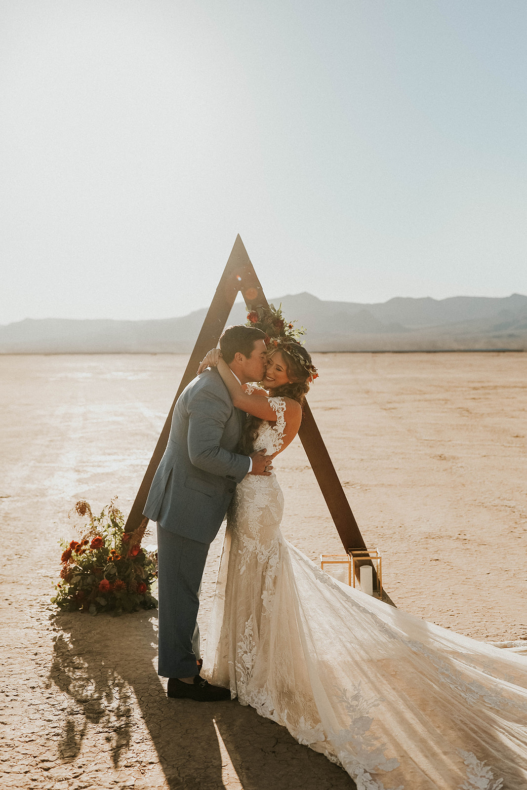 Groom Kisses Bride on Cheek under Triangle Arch after Ceremony for Dry Lake Bed Fall Inspired Elopement 