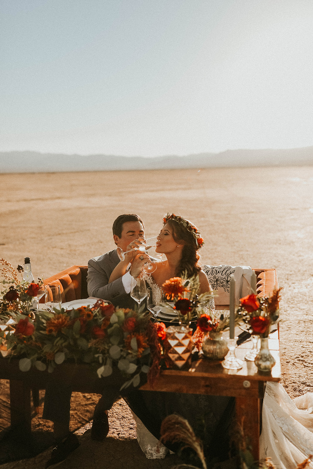 Newlyweds Drinking Champagne while Sitting at Dry Lake Bed Fall Inspired Elopement Sweetheart Table with Velvet Couch & Fall Inspired Floral 