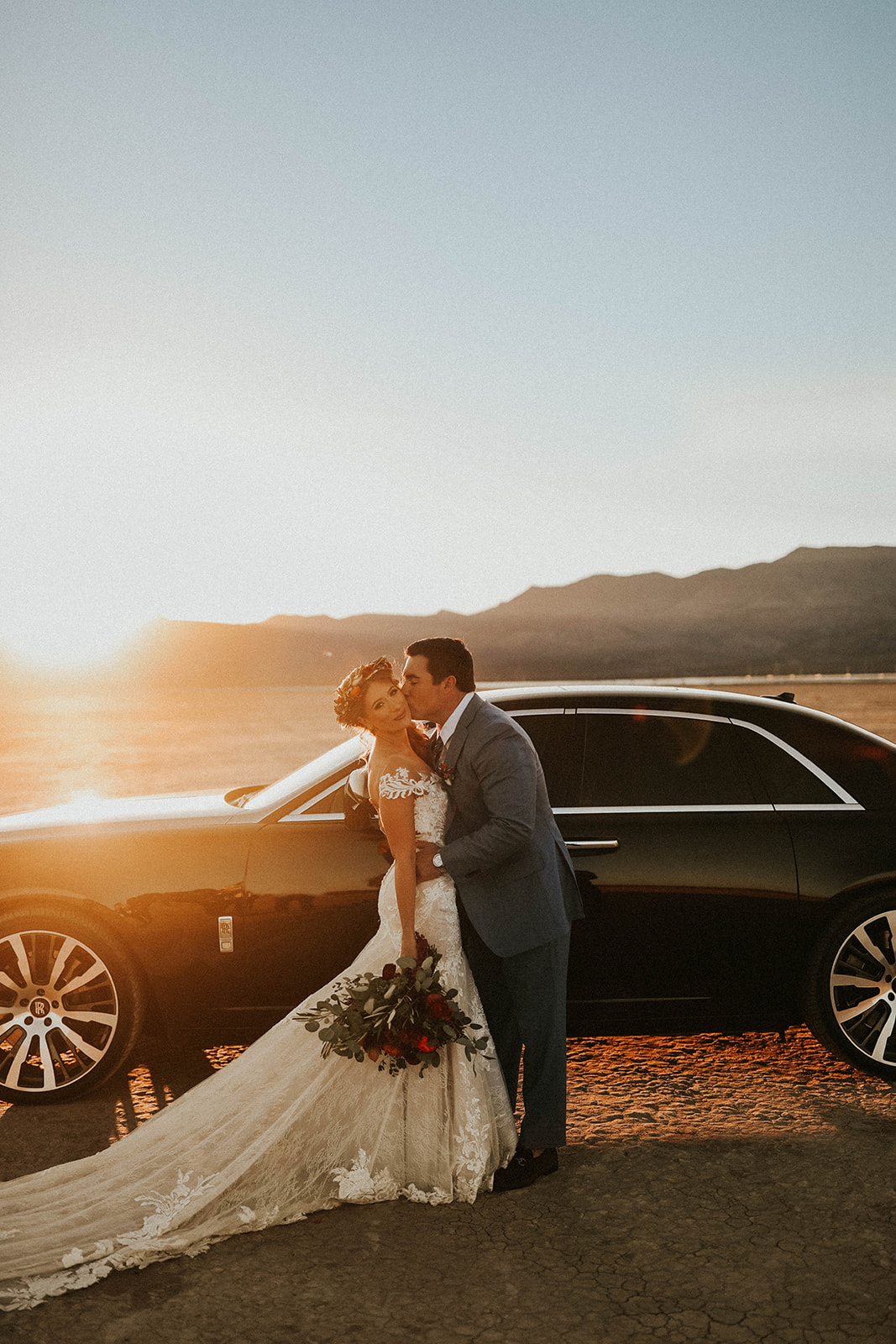 Groom Kissing Bride on Cheek in front of Rolls Royce on Dry Lake Bed 