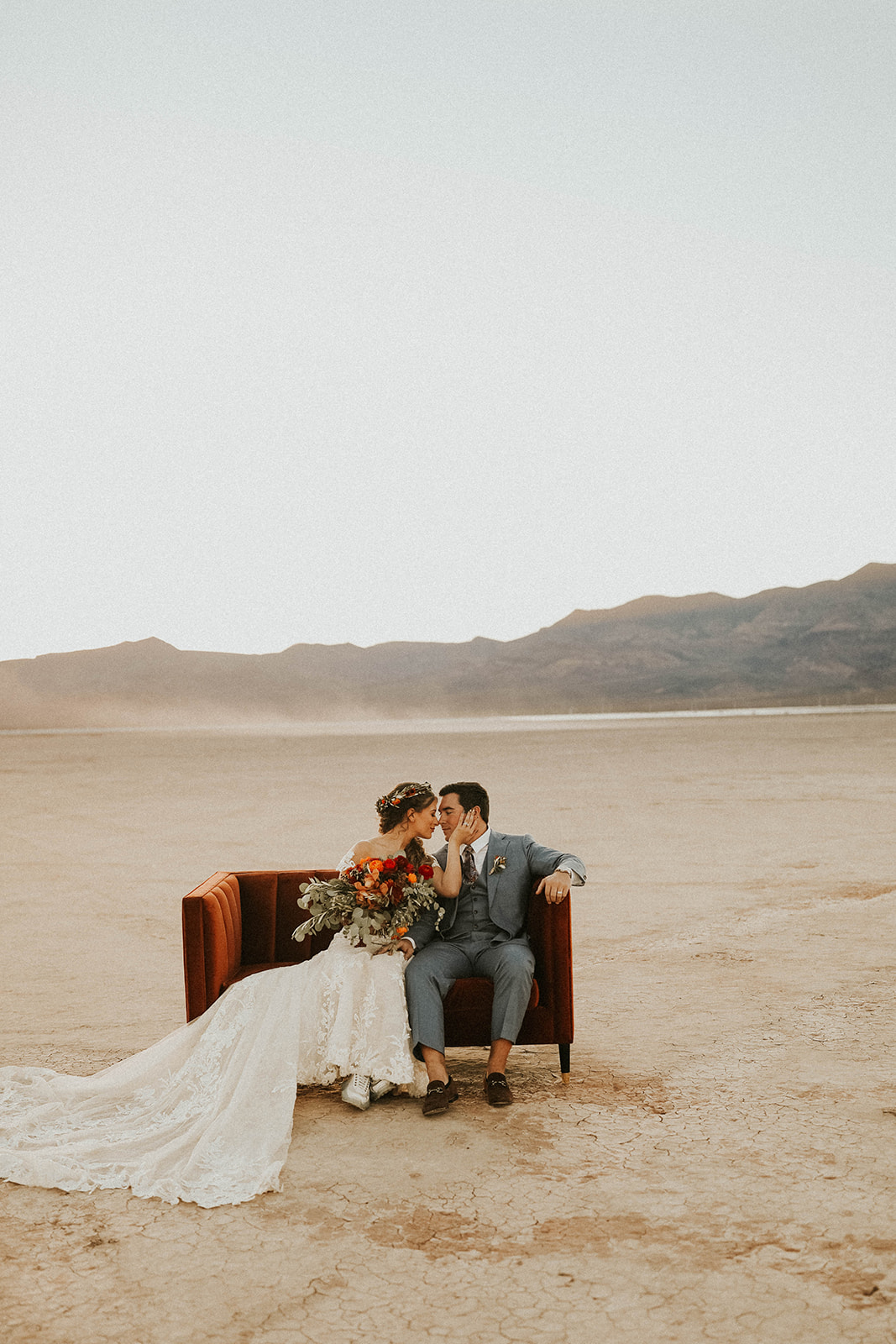 Newlyweds sitting on Velvet Couch Touching Noses during Sunset in Dry Lake Bed Fall Inspired Elopement in Las Vegas