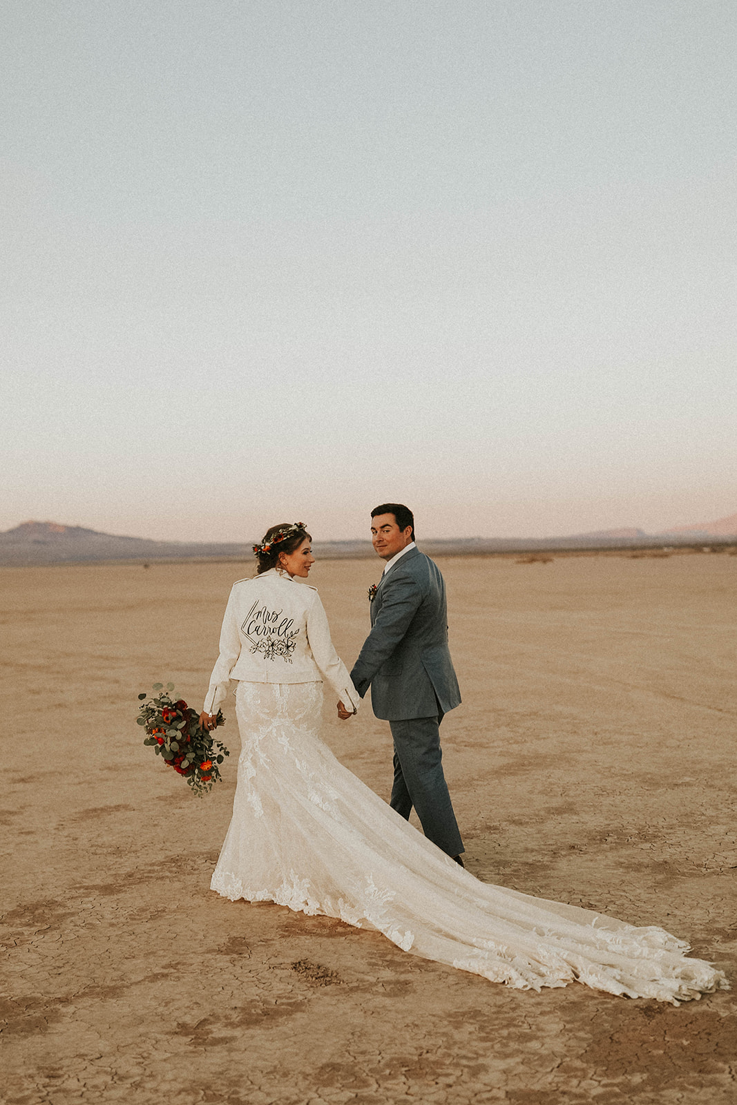 Bride in Custom Bridal Jacket & long train walking with Groom on Dry Lake Bed in Las Vegas at Dry Lake Bed Fall Inspired Elopement