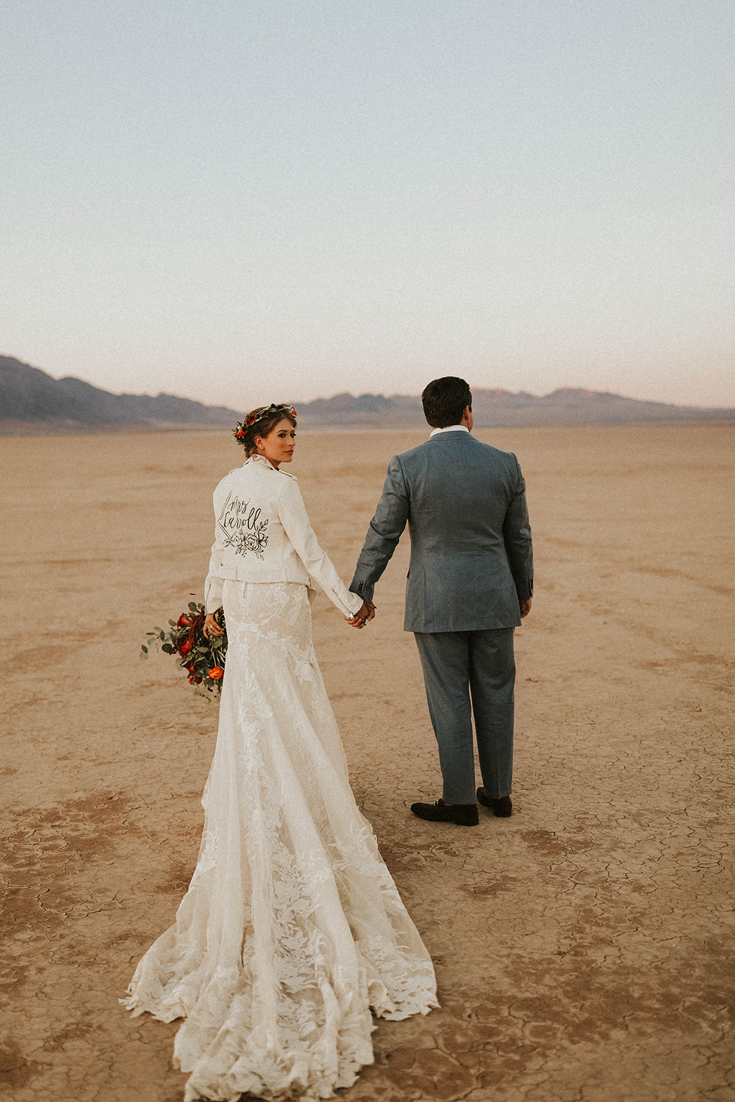 Bride in Custom Bridal Jacket & long train looking back and walking away with Groom at Dry Lake Bed Fall Inspired Elopement