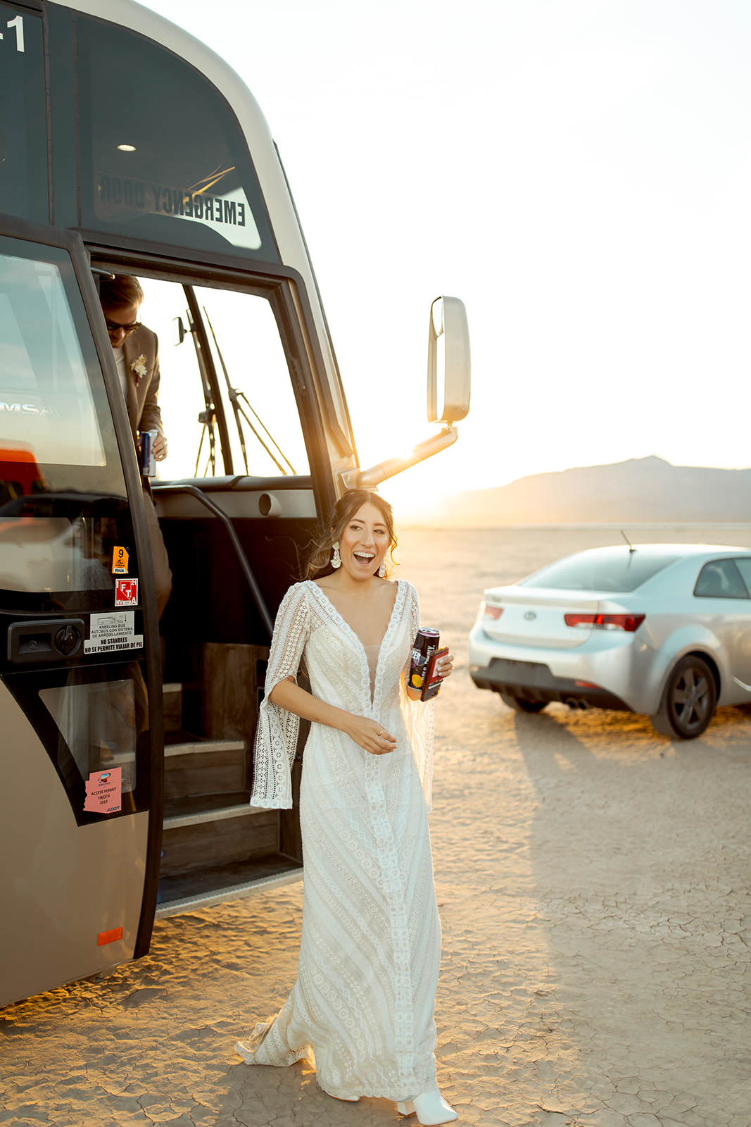 Bride in boho lace dress stepping off bus and reacting to reception on Dry Lake Bed 