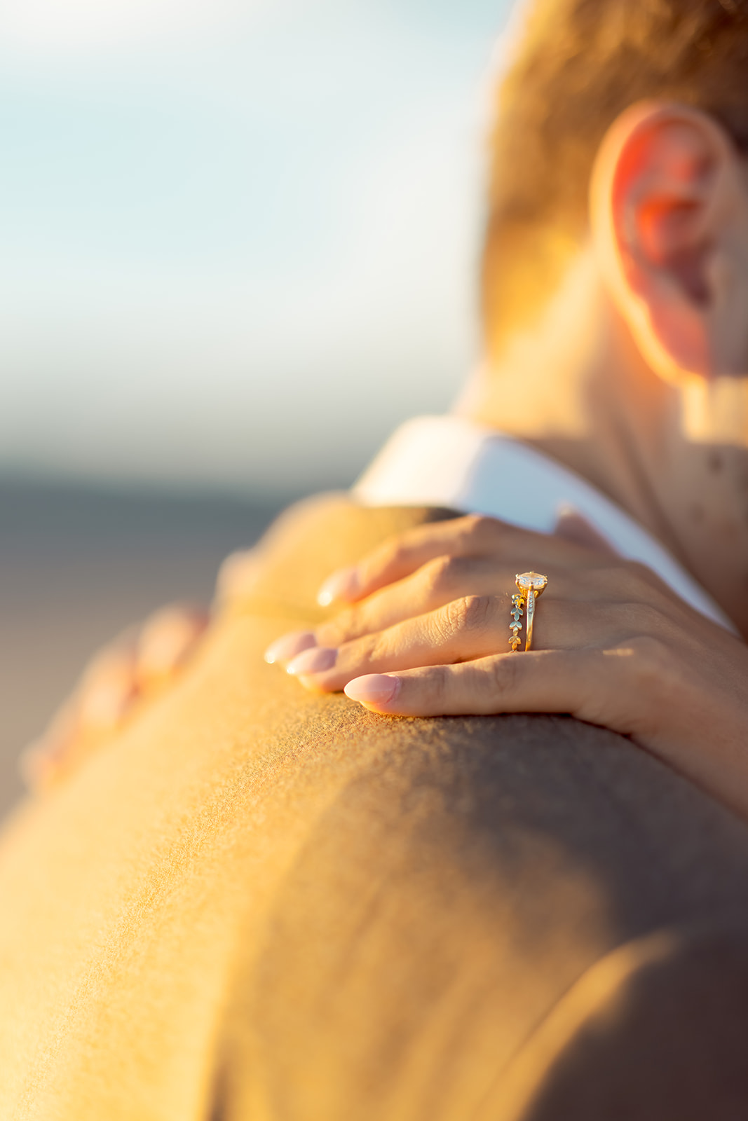 Brides hand with Wedding Ring on Grooms Shoulder during Sunset 
