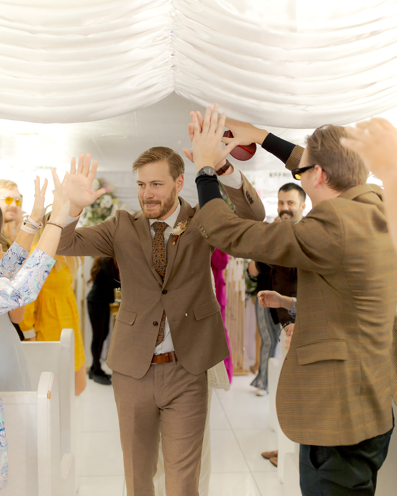 Groom in vintage brown suit giving guests high fives after wedding  ceremony 