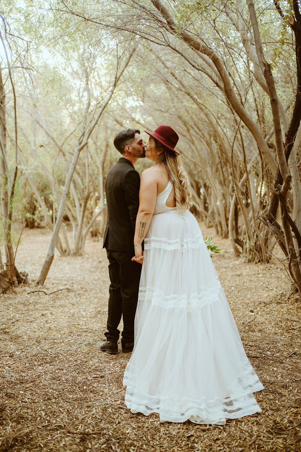 Groom Kissing Bride in Burgundy Felt Hat in Olive Grove in Las Vegas 
