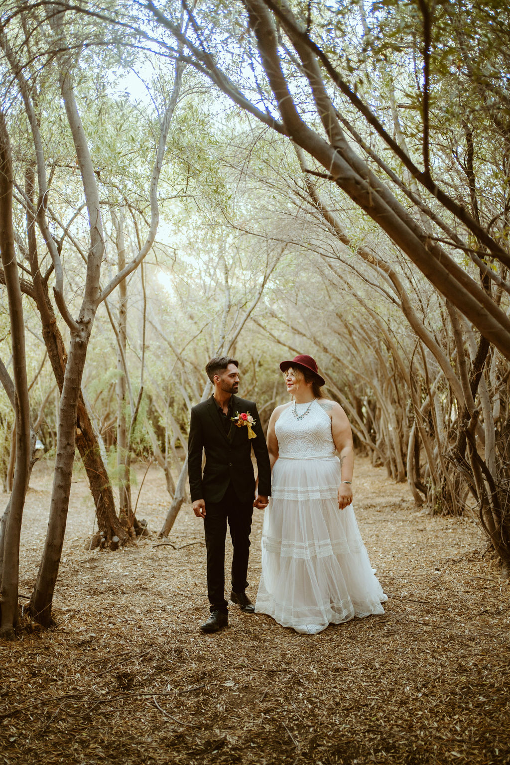 Groom walking with Bride in Burgundy Felt Hat in Olive Grove after Elopement at GreenGale Farms 