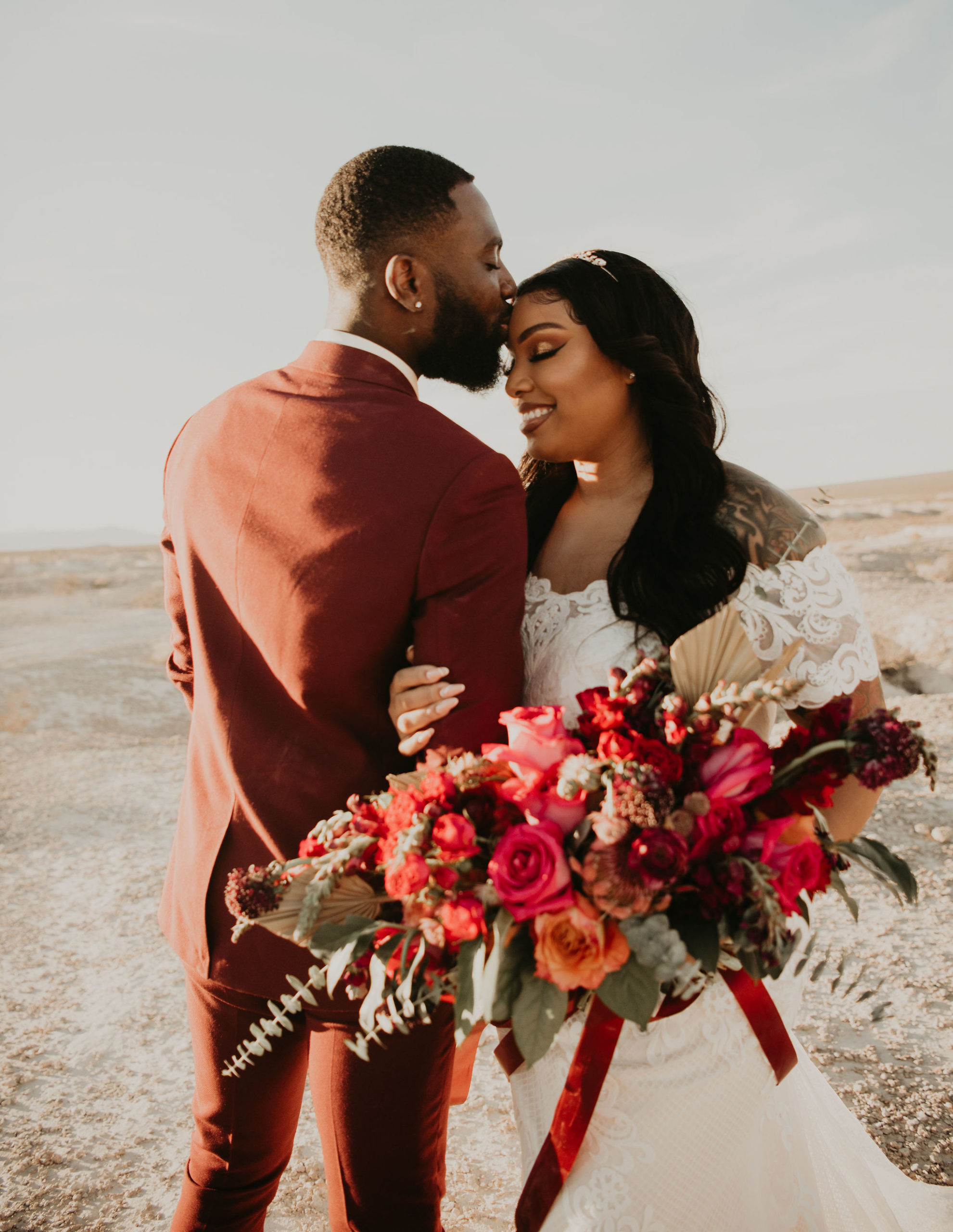 Groom Kissing Bride with Glam Make-up & Jewel Tone Bouquet in Desert 