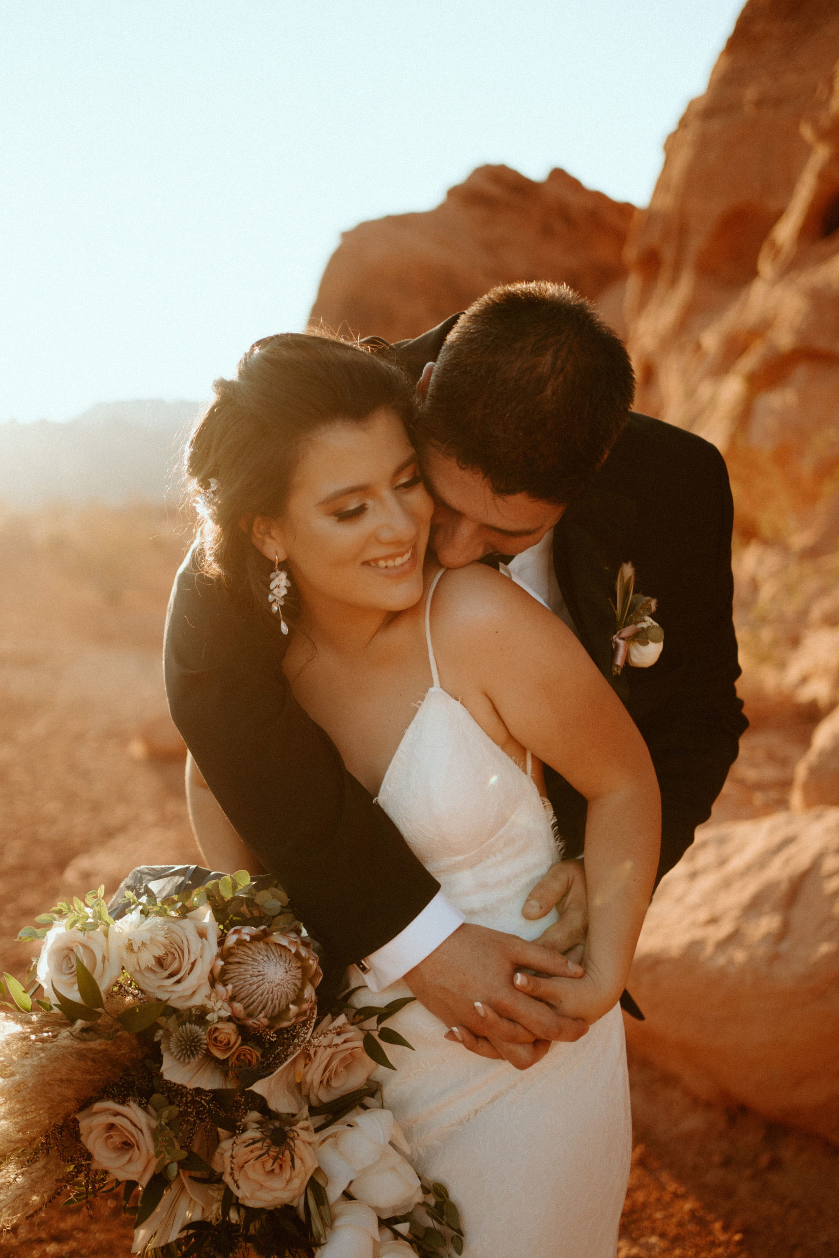 Groom Holding Bride and Kissing Shoulder during Sunset 